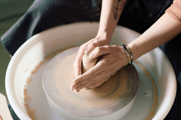 High angle closeup of hands of unrecognizable female potter shaping clay on wheel in workshop