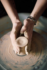 Vertical from above view of hands of unrecognizable female potter shaping clay on wheel in workshop