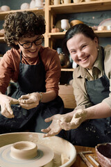 Vertical shot of cheerful woman with Down syndrome and her female friend enjoying pottery class...