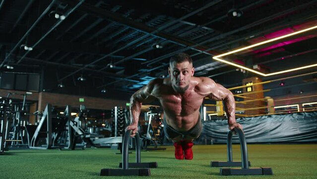 In a contemporary fitness center, a man showcases his commitment to health with rigorous pushup workouts using parallettes, emphasizing strength and dedication to physical wellbeing