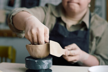 Closeup of hands of unrecognizable woman with Down syndrome making ceramic bowl in pottery class