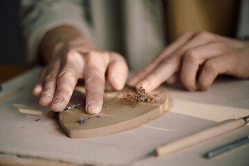 Closeup shot of hands of unrecognizable female artisan pressing dried flowers onto ceramic leaf...