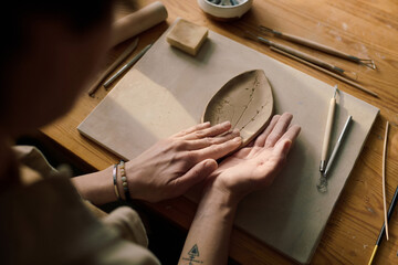 High angle view of hands of unrecognizable female artisan shaping ceramic leaf plate