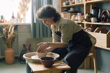 Mature Caucasian female artisan creating bowl on potters wheel in modern workshop, copy space
