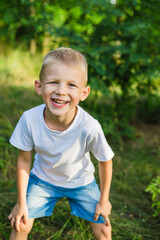 A young boy is smiling and laughing against a backdrop of lush green forest. His joyful expression radiates happiness.