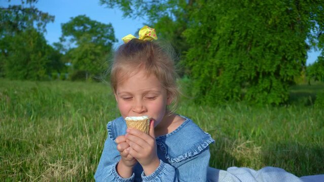 A girl eats ice cream with strawberriy in the park. The girl put a strawberry on the ice cream and bites it.