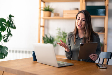 Smiling female entrepreneur discussing over video call on laptop while sitting at desk in home...