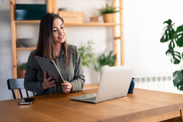 Smiling female entrepreneur discussing over video call on laptop while sitting at desk in home office.