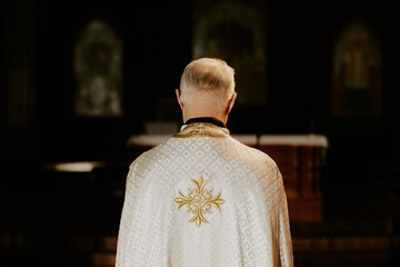 Back view of unrecognizable senior Catholic priest wearing chasuble standing indoors, copy space