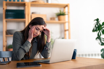 Young businesswoman sitting at desk in home office having tired look, having pain, being sleepy and...
