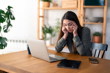 Serious pensive woman suffering from headache distantly working from home office or studying for exam.