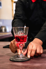 vertical red cocktail with alcohol in a glass tumbler delivered by a woman's hands - drink concept