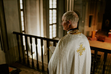 High angle view of senior Catholic priest holding prayer book standing at mezzanine in church, copy...