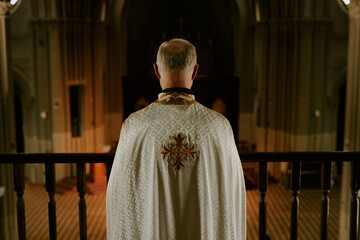 Rear view of unrecognizable senior Catholic priest wearing vestment standing at mezzanine in church