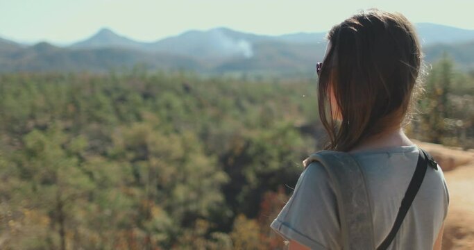 A woman standing confidently on the edge of a cliff, overlooking a vast landscape below. Her hair blows in the wind as she takes in the stunning view.