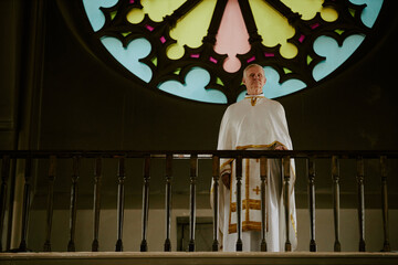 Wide shot of senior Caucasian Catholic priest wearing liturgical vestment standing at mezzanine in...