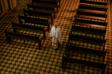 High angle view wide shot of senior Caucasian priest walking along Catholic church nave, copy space