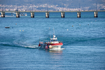 A small fishing boat returns to the port of Canido with the Toralla bridge in Vigo, Pontevedra,...