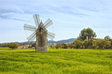 Ancient windmill on green meadow with blue sky and hill at background, Mallorca. Famous tourist attractions in Mallorca - over 5000 windmills all over the island
