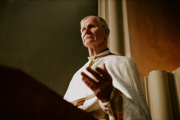 Low angle view medium shot of elderly Caucasian priest preaching sermon in Catholic church, copy...