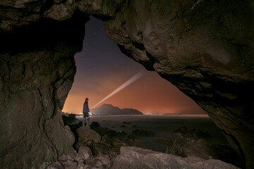A fisherman at night lights up the sky with his flashlight from a natural cave on the beach of Berria, Cantabria