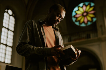 Low angle view medium shot of African American man standing in Catholic church reading religious...