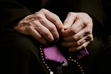 Closeup of wrinkled hands of unrecognizable elderly Catholic priest holding rosary