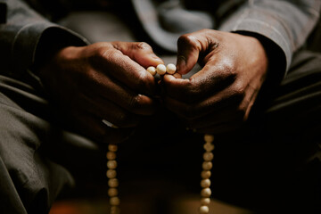 Closeup shot of unrecognizable African American male parishioner praying with rosary in hands