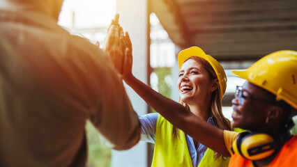 A joyful team of multiethnic construction workers, wearing helmets and safety vests, engages in a...