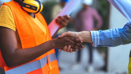 Two diverse women in construction attire engage in a handshake, symbolizing collaboration and...