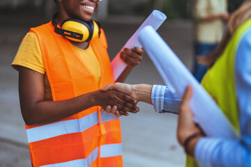 Two female construction professionals in reflective vests and safety gear shake hands at a building...