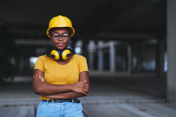 A professional black female construction worker stands proudly with crossed arms wearing protective...
