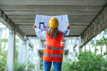 Caucasian woman in safety gear examines construction plans at a building site, showcasing industry...