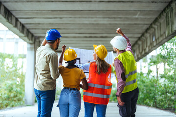 A group of male and female construction professionals from diverse backgrounds reviews a building...