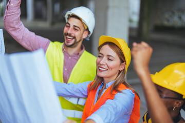 A group of cheerful diverse construction workers, clad in bright safety vests and hard hats,...