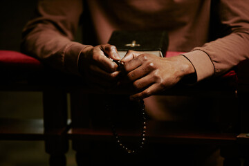 Hands of unrecognizable Black man holding rosary praying in Catholic church, copy space