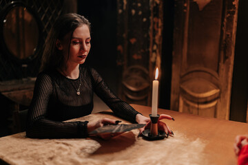Portrait of mysterious fortuneteller shuffling tarot cards during magic ritual in dark room by...