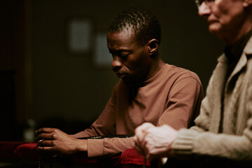 Selective focus shot of senior Caucasian and young Black men holding rosary praying during service...