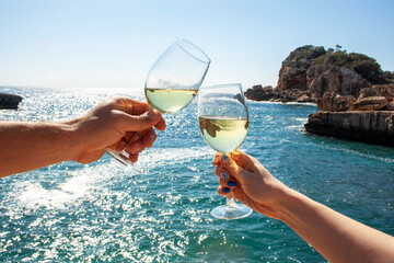Two hands, male and female, hold glasses of champagne against the backdrop of the sea and mountains. Vacation, travel concept