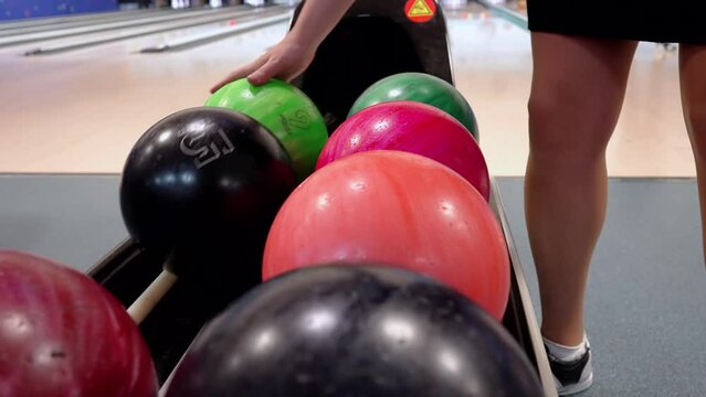  A variety of brightly coloured bowling balls neatly arranged on a roller stand in a bowling alley.