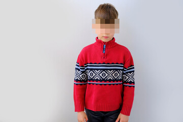 offended or punished child, a boy of 7-8 years old in a red Scandinavian sweater, kid's face is...