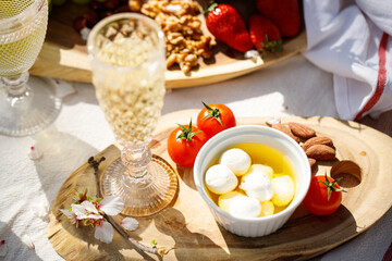 Picnic with wine, cheeses and fruits in the spring garden on a light tablecloth on a sunny day, almond blossoms. Shavuot, brunch.