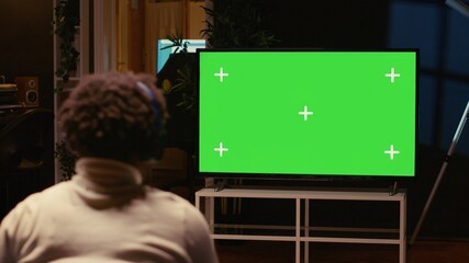 Man playing singleplayer videogames on green screen TV in cozy living room used as home theatre....