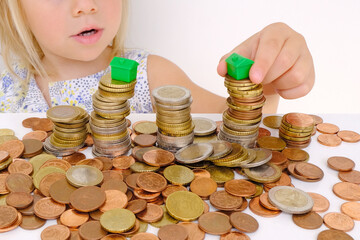 house model on stacks euro currency coins, small child, blonde girl 3 years old playing with cash,...