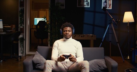 BIPOC man using headphones mic to discuss strategies with teammates while playing videogame in cozy...
