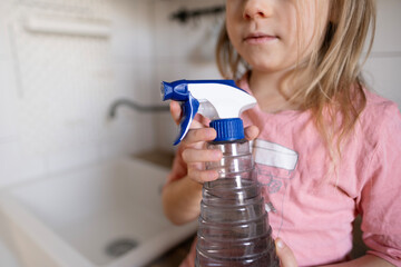 cleaning spray bottle detergent for various surfaces in kitchen in children's hands close-up,...