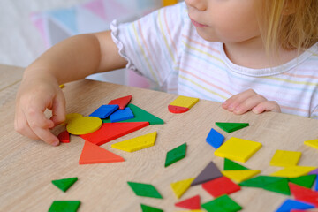 child, toddler, girl plays with colored wooden geometric figures, cubes, builds houses and animals,...