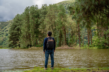 Young man meditating and contemplating nature in front of a lake and pine forest.
