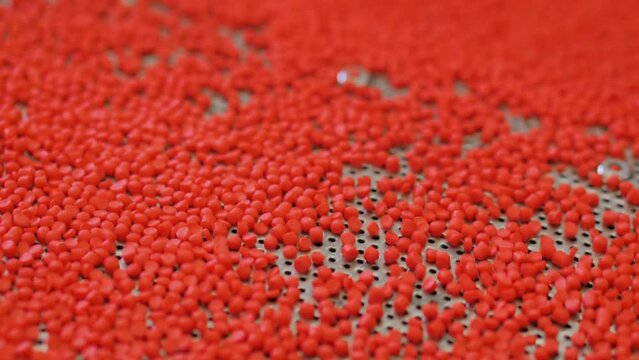 Plastic recycling machine: bouncing red recycled pellets, granules on vibrating shale shaker, conveyor at factory: close up, selective focus. Separation, sustainable and waste reduction concept