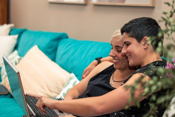 Homosexual girls couple embracing and having fun with laptop spending time together on home sofa